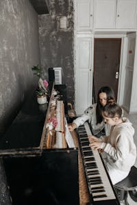 A young girl receiving personalized piano instruction from an adult teacher indoors.