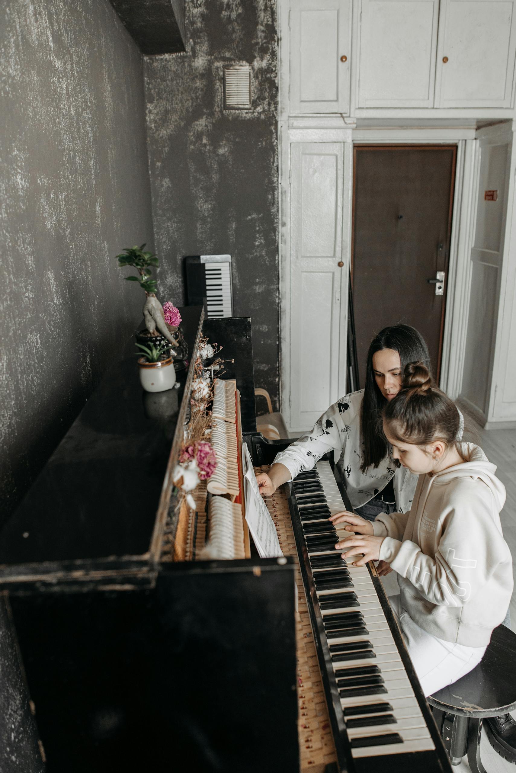 A young girl receiving personalized piano instruction from an adult teacher indoors.