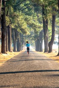 A woman runs along a serene, tree-lined road in a picturesque park setting, illustrating fitness and tranquility.