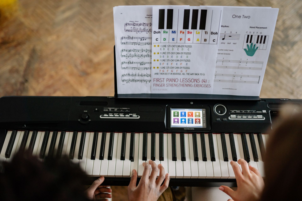 Adults work through music with sheet music at the piano, viewed from above.
