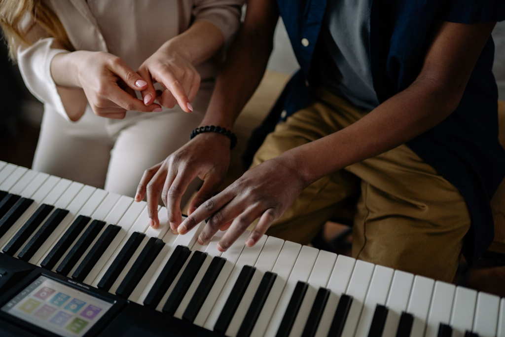 A close-up of a teacher and student during a piano lesson, focusing on hand placement.