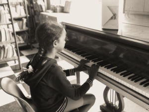A young girl practices piano indoors in a cozy home setting, focused and serene.